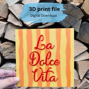 May include: A square sign featuring a yellow background with vertical orange stripes and the red text La Dolce Vita in a cursive script. The sign is labeled as a 3D print file and a digital download, indicating it is a design for printing.