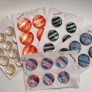Op de afbeelding: Assortiment van kleurrijke knopen met verschillende patronen en ontwerpen. De knopen zijn gerangschikt op wit karton met het woord "Bardillo" en een nummer gedrukt op elke kaart.