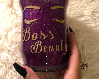 May include: Purple glitter makeup brush holder with gold glitter eyelashes and the text "Boss Beauty".