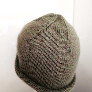 Peut inclure: Un bonnet tricoté dans une teinte vert olive sourd avec de subtiles taches multicolores dans le fil. Le chapeau présente un motif de côtes verticales sur le corps principal, une couronne structurée avec des lignes de diminution et un bord roulé.