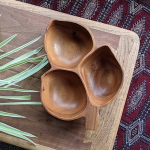 May include: A wooden serving dish with three separate bowls. The dish is made of dark brown wood and has a natural finish. The bowls are all the same size and shape, and they are arranged in a triangular pattern.