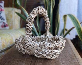 May include: A white wicker basket with a woven handle. The basket is sitting on a wooden table.