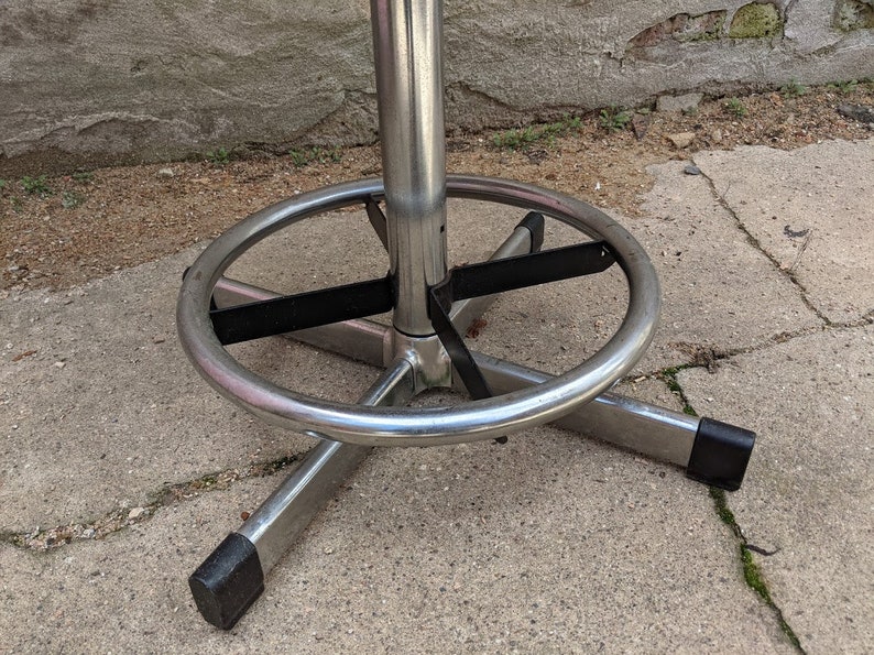 May include: Close-up of a chrome bar stool base with a black metal ring and a footrest. The stool has a swivel base and is designed for use in a bar or kitchen setting.