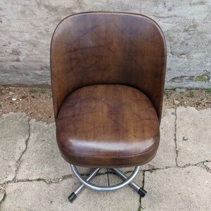 May include: A brown leather swivel chair with a chrome base. The chair has a rounded back and seat.