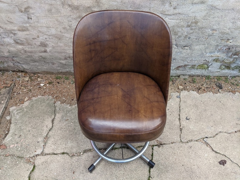 May include: A brown leather swivel chair with a chrome base. The chair has a rounded back and seat.