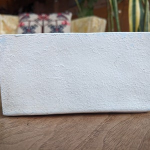 May include: A white rectangular planter with a textured surface. The planter is made of a durable material and is perfect for displaying small plants or succulents.