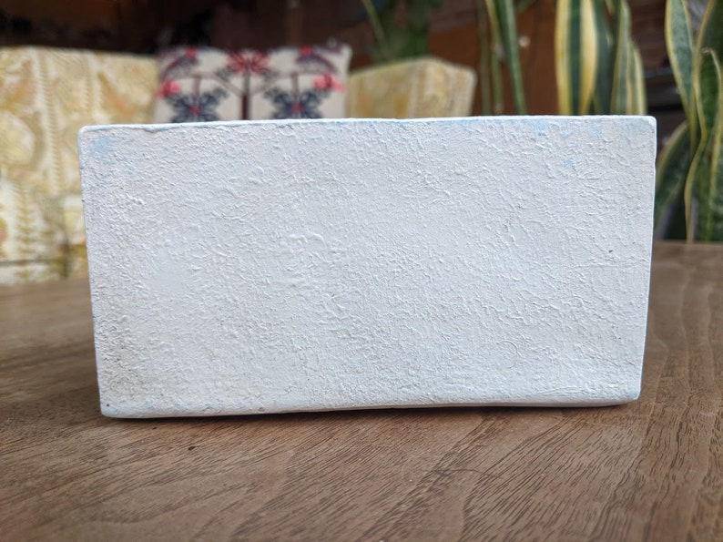May include: A white rectangular planter with a textured surface. The planter is made of a durable material and is perfect for displaying small plants or succulents.