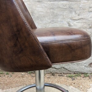 May include: A brown leather swivel chair with a metal base. The chair has a tufted seat and a curved back.
