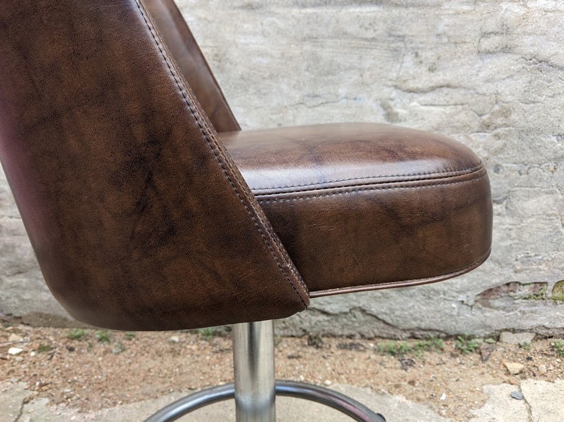 May include: A brown leather swivel chair with a metal base. The chair has a tufted seat and a curved back.