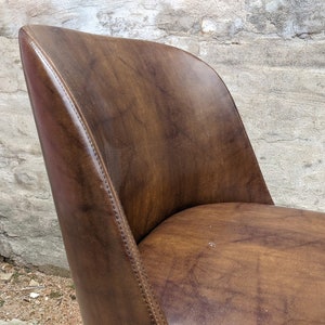 May include: A brown leather chair with a curved back and a slightly rounded seat. The chair has a stitched seam along the back and sides.