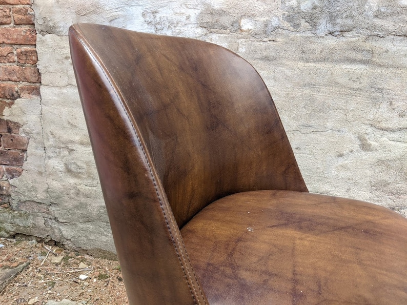 May include: A brown leather chair with a curved back and a slightly rounded seat. The chair has a stitched seam along the back and sides.