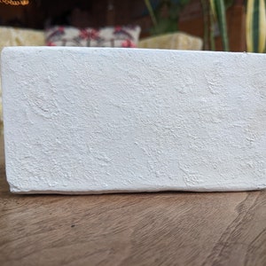 May include: A white rectangular planter with a textured surface. The planter is made of a rough material and has a slightly uneven surface.