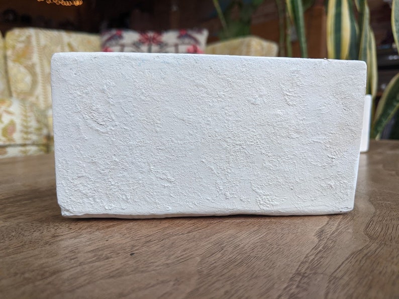 May include: A white rectangular planter with a textured surface. The planter is made of a rough material and has a slightly uneven surface.