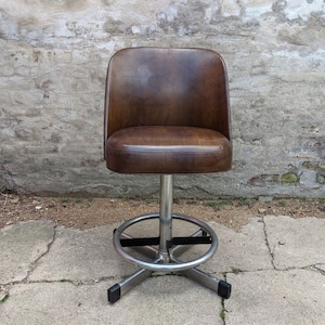 May include: A brown leather swivel bar stool with a chrome base and footrest. The stool has a rounded back and a comfortable seat.