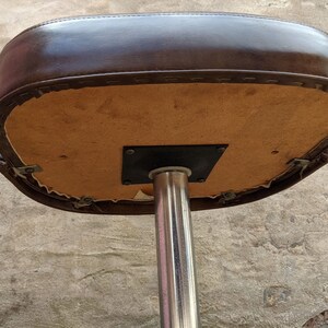 May include: The underside of a brown leather bar stool with a chrome base. The seat is attached to the base with a metal plate.