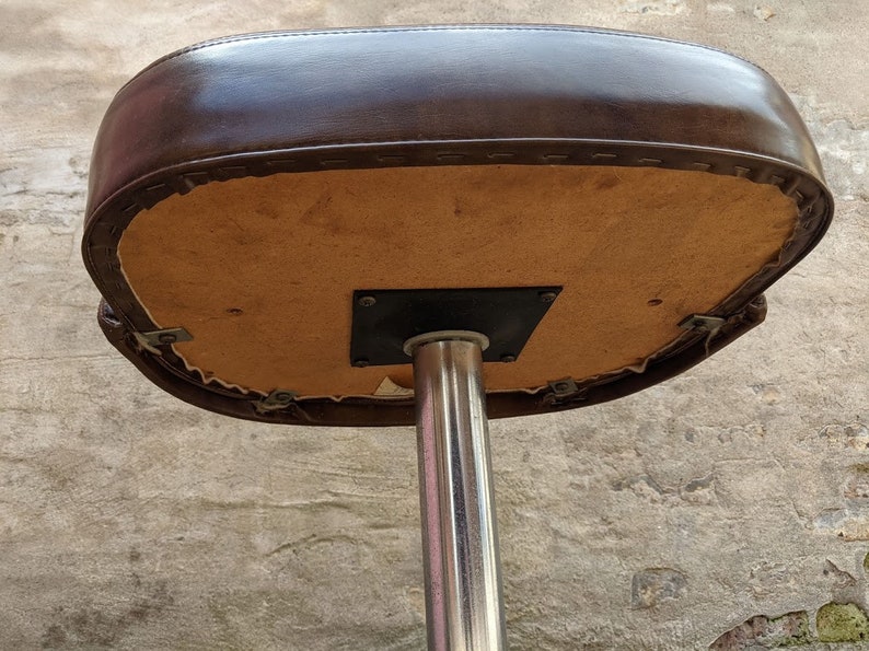 May include: The underside of a brown leather bar stool with a chrome base. The seat is attached to the base with a metal plate.