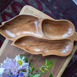 May include: A wooden serving dish shaped like a leaf with three separate compartments. The dish is made of light brown wood and has a smooth, polished finish.