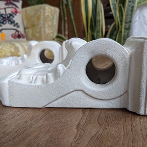 May include: Three white ceramic shelf brackets with intricate details and a round hole in the center. The brackets are designed to support shelves or other decorative items.