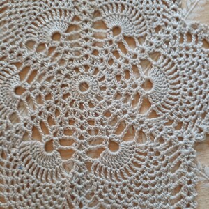 May include: Close-up of a beige crocheted doily with a circular pattern.