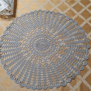 May include: A gray crocheted doily with a delicate pattern. The doily is circular and has a scalloped edge.