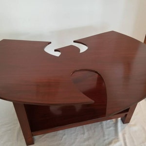 May include: A dark brown wooden coffee table with a unique cutout design in the shape of the Wu-Tang Clan logo. The table has a lower shelf for storage.