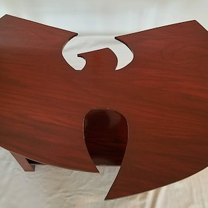May include: A dark red wooden coffee table shaped like the Wu-Tang Clan logo. The table has a smooth, polished finish and a cutout in the center.