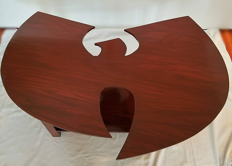 May include: A dark red wooden coffee table shaped like the Wu-Tang Clan logo. The table has a smooth, polished finish and a cutout in the center.