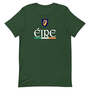 Puede incluir: Una camiseta verde con un gráfico blanco de un arpa y la palabra "ÉIRE" en blanco con una franja verde, blanca y naranja debajo.