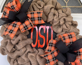 May include: A burlap wreath with two black and orange plaid bows and a black sign with the word "BOO" in orange letters.