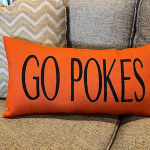 K&ouml;nnte beinhalten: Orangefarbener Dekokissen mit schwarzem Text "GO POKES".