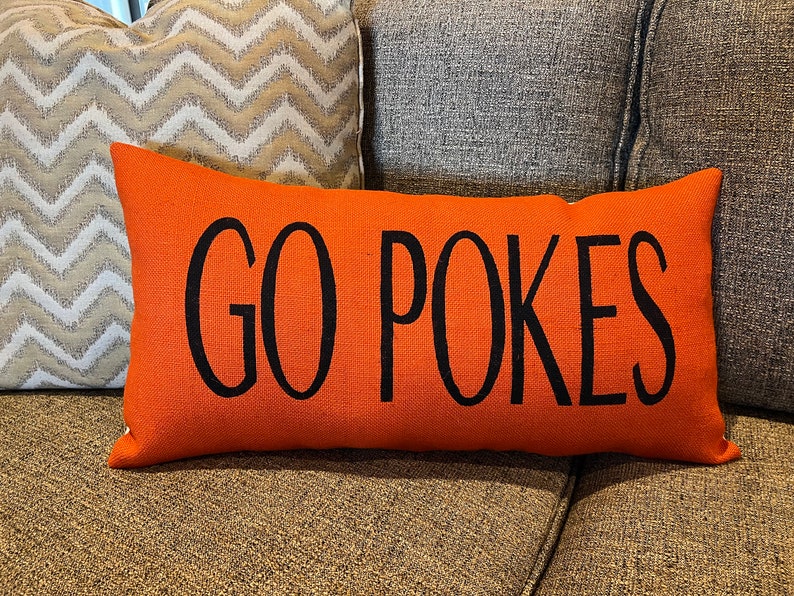 K&ouml;nnte beinhalten: Orangefarbener Dekokissen mit schwarzem Text "GO POKES".