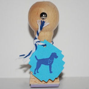 Könnte beinhalten: Ein Holz-Stempel mit einem blau-weißen Seil, das um den Griff gebunden ist. Der Stempel zeigt eine blaue Silhouette eines Hundes mit einem Herzen auf der Brust auf türkisfarbenem Hintergrund.
