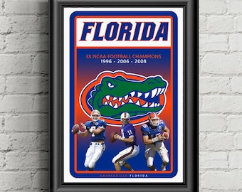 May include: Framed print featuring the word "FLORIDA" in orange and blue, with the text "3X NCAA FOOTBALL CHAMPIONS 1996-2006-2008." The image includes a green alligator graphic and three football players in uniform.