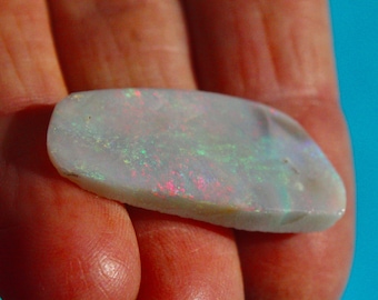 May include: A white opal gemstone with iridescent flashes of green, red, and blue. The opal is oval shaped and has a smooth, polished surface.