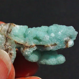 May include: A cluster of light blue, green, and white mineral crystals with brown veins. The crystals are clustered together in a rough, organic shape.