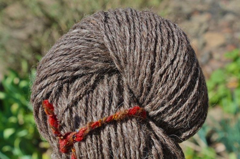 May include: A close-up of a brown yarn ball with a red and orange ribbon tied around it.