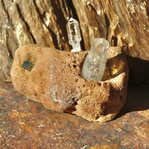 May include: Two clear quartz crystals and a dark blue crystal are nestled in a brown, porous rock.