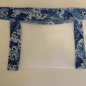 May include: A rectangular laundry bag with a white mesh body and a blue fabric border. The fabric border features a repeating pattern of white waves on a dark blue background. The bag is designed for washing delicate items.