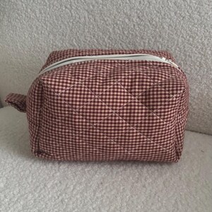 K&ouml;nnte beinhalten: Eine gesteppte Kosmetiktasche mit burgunderrotem und rosa Vichy-Muster und einem wei&szlig;en Rei&szlig;verschluss. Die Tasche hat eine kleine Stoffschlaufe. Ma&szlig;e in Zentimetern.