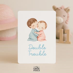 May include: A white card with the text "Double Trouble" in light blue script. The card features an illustration of two babies hugging, one in blue and the other in pink. The Cute Pixels logo is at the bottom.