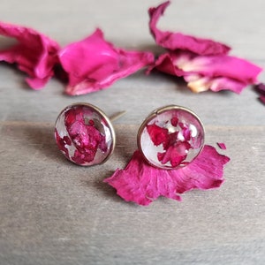 Op de afbeelding: Een paar gouden oorbel studs met roze bloemblaadjes ingekapseld in helder hars.