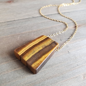 May include: A gold chain necklace with a large, rectangular tiger's eye pendant. The pendant has a brown, gold, and black striped pattern.