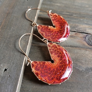 May include: A pair of gold hoop earrings with a red and orange mandala design. The earrings are made of metal and have a circular shape.