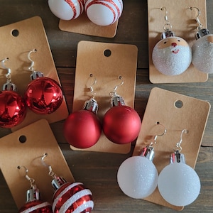 Puede incluir: Surtido de pendientes de adorno navideño. Los pendientes están hechos de adornos de purpurina blanca, roja y plateada. Algunos adornos tienen rayas rojas y blancas. Algunos adornos tienen una cara de Papá Noel.