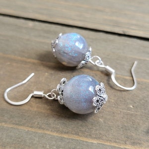 May include: A pair of silver dangle earrings with a gray and silver glitter ball charm. The ball charm has a silver filigree design.