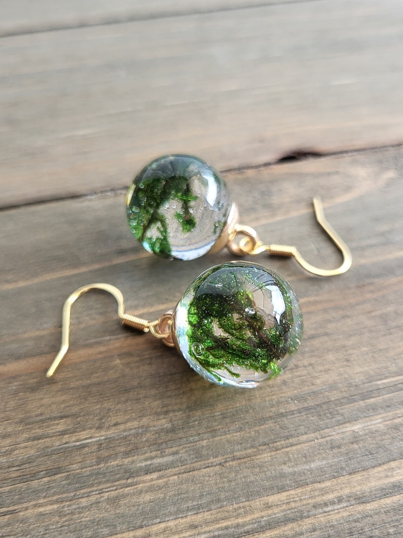 May include: A pair of gold earrings with clear glass orbs containing preserved green moss.