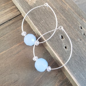 Puede incluir: Un par de pendientes de aro de plata con cuentas facetadas de color azul claro y cuentas de cristal transparente.