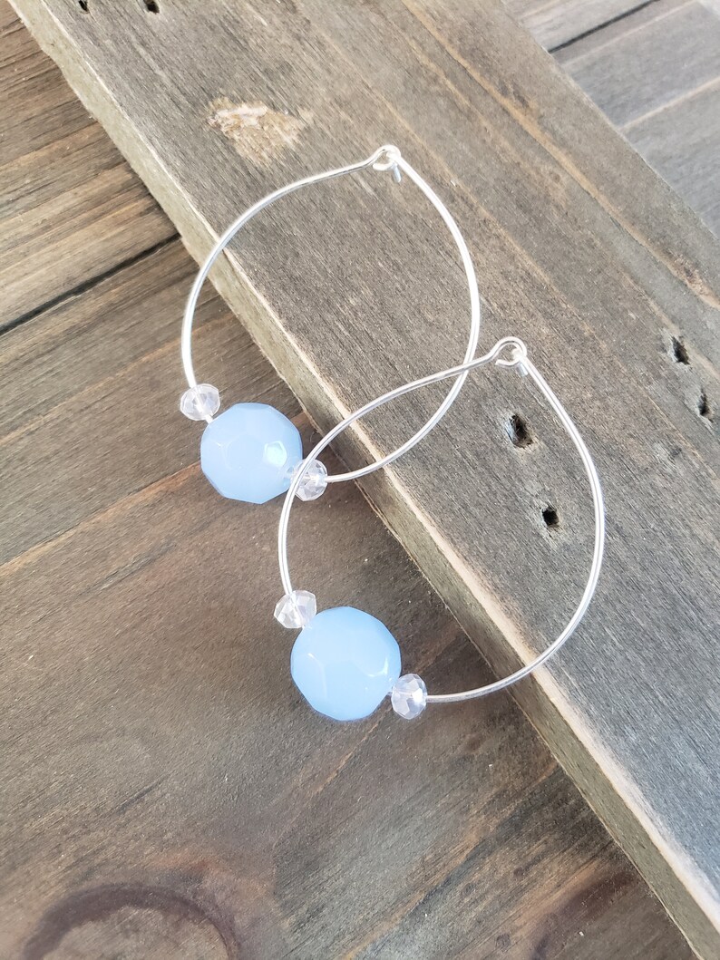 Puede incluir: Un par de pendientes de aro de plata con cuentas facetadas de color azul claro y cuentas de cristal transparente.