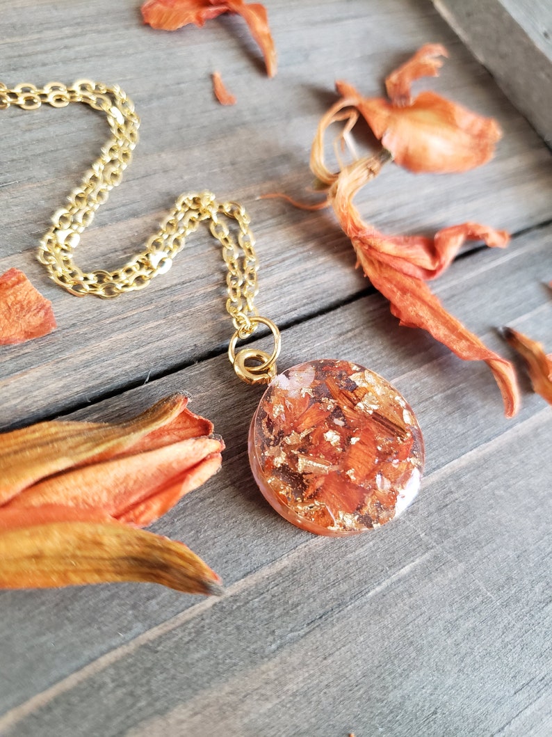 May include: A gold chain necklace with a round pendant featuring dried orange flower petals and gold leaf encased in clear resin.