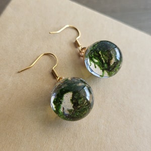 May include: A pair of gold dangle earrings with clear glass spheres containing preserved green moss.